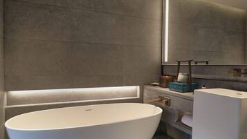 A modern bathroom with a freestanding bathtub, a mirror, and a countertop with toiletries.