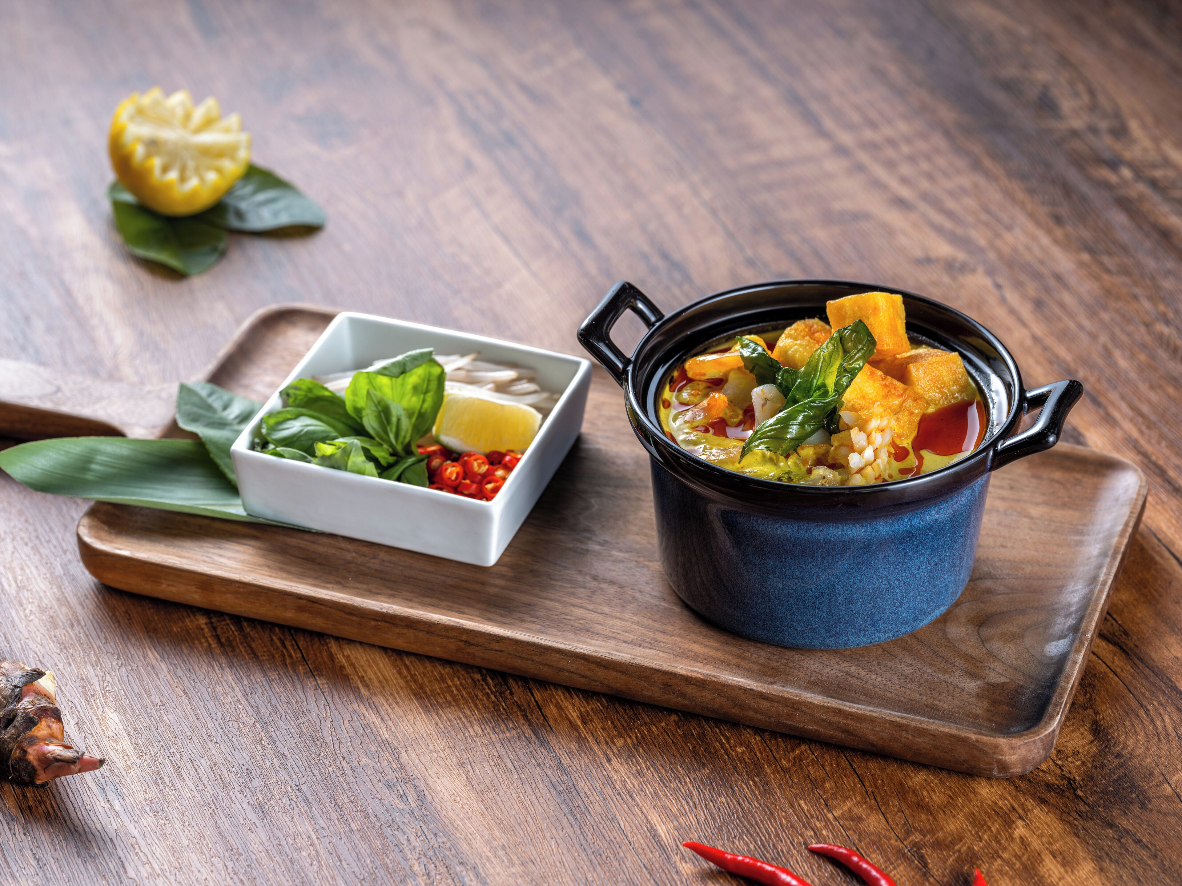 A wooden tray with a bowl of soup and a small bowl of condiments.