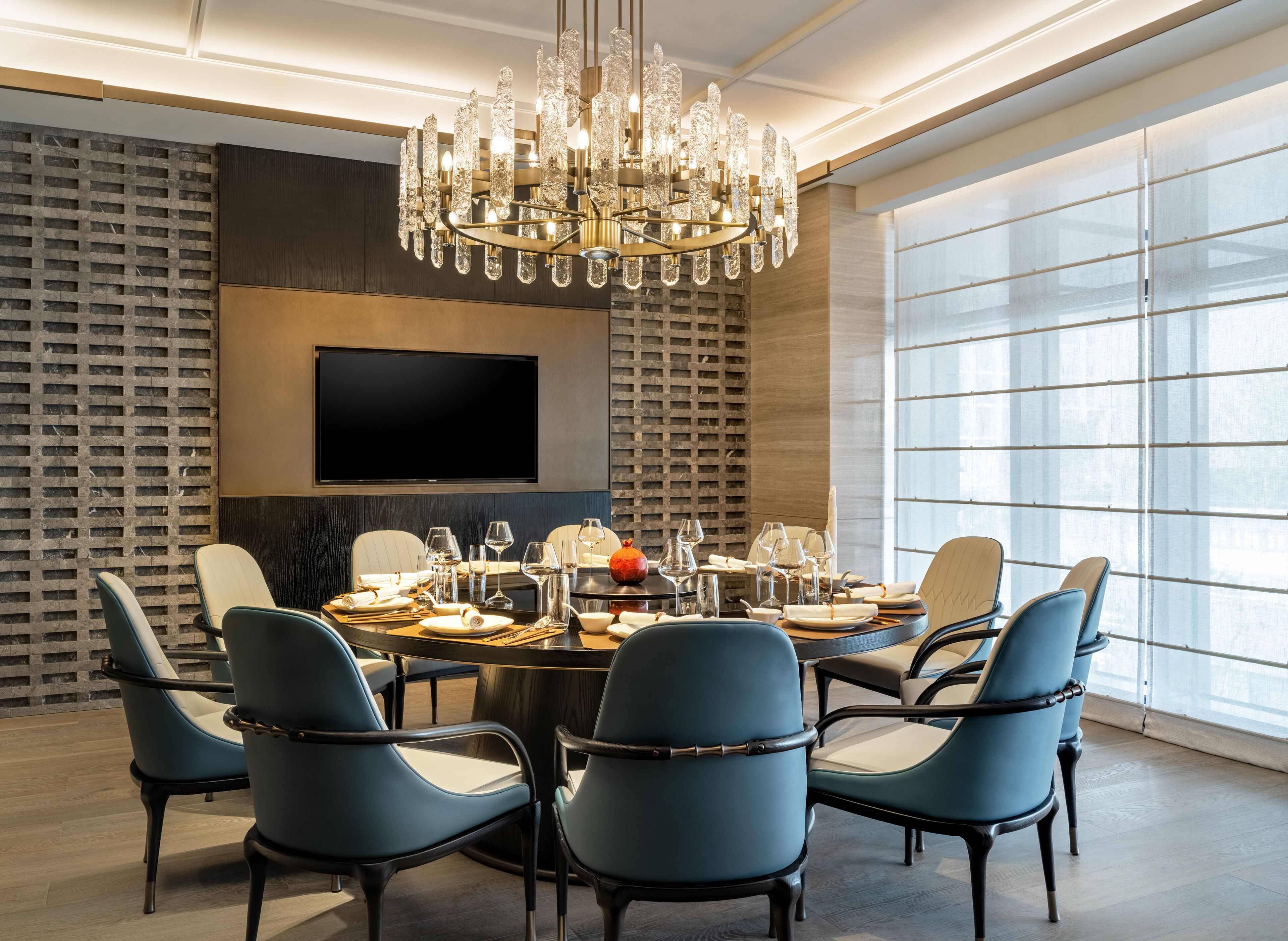 A modern dining room with a chandelier, a large flat-screen TV, and a round table set for six.