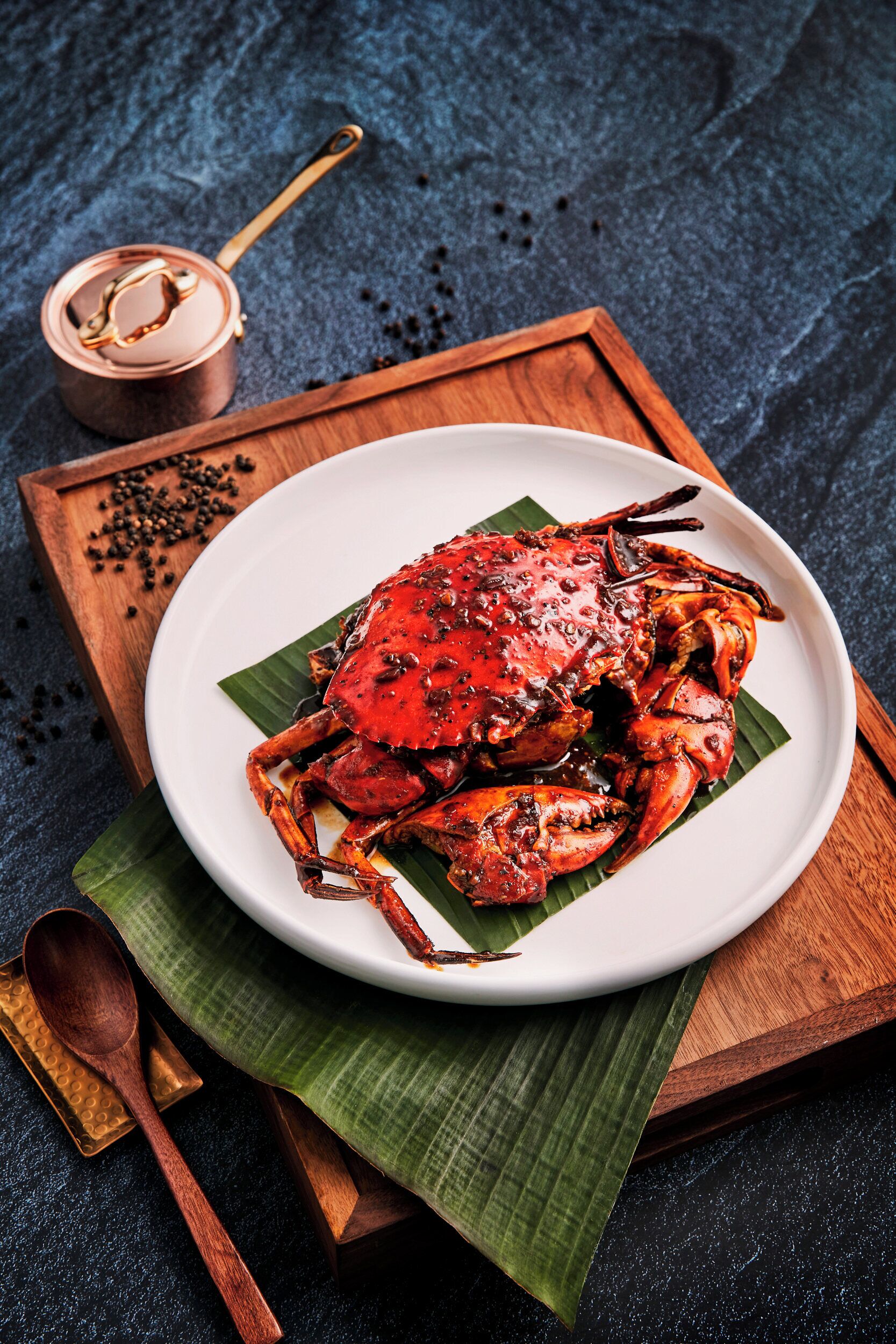 A plate of cooked crab on a white plate with a banana leaf underneath, placed on a wooden tray.