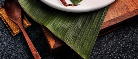 A plate of cooked crab on a white plate with a banana leaf underneath, placed on a wooden tray.