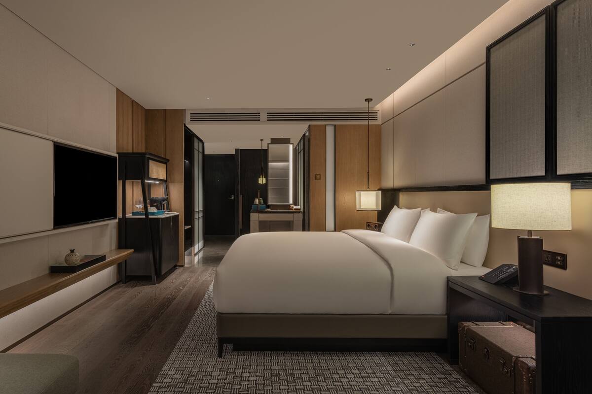 A modern hotel room with a large bed, bedside tables, a TV, and a desk.
