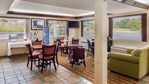 A hotel room with a dining area, a sofa, a clock, and a TV.