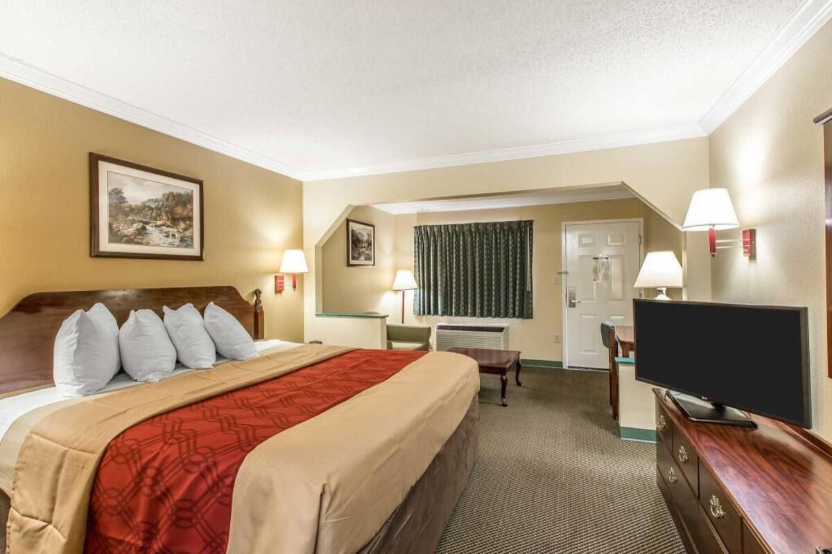 Habitación de hotel con cama, televisión, escritorio y baño visible a través de una puerta abierta.