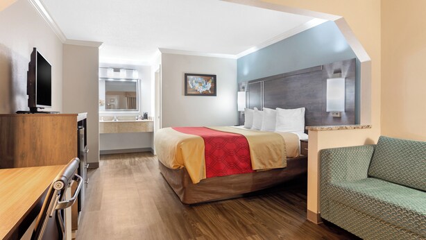 A hotel room with a bed, a green sofa, a wooden desk, and a television.