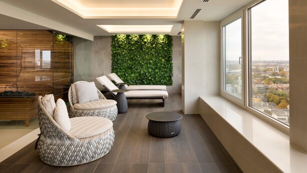 A modern lounge area with wicker furniture, a green wall, and a city view. - Radisson Blu Hotel Olumpia (Tallinn)