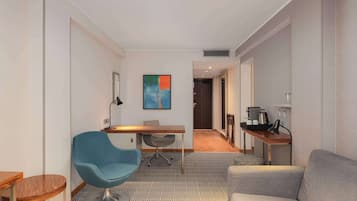 Une chambre d’hôtel moderne avec un fauteuil bleu, un canapé gris, une table basse en bois et un coin repas comprenant une petite table et des chaises.