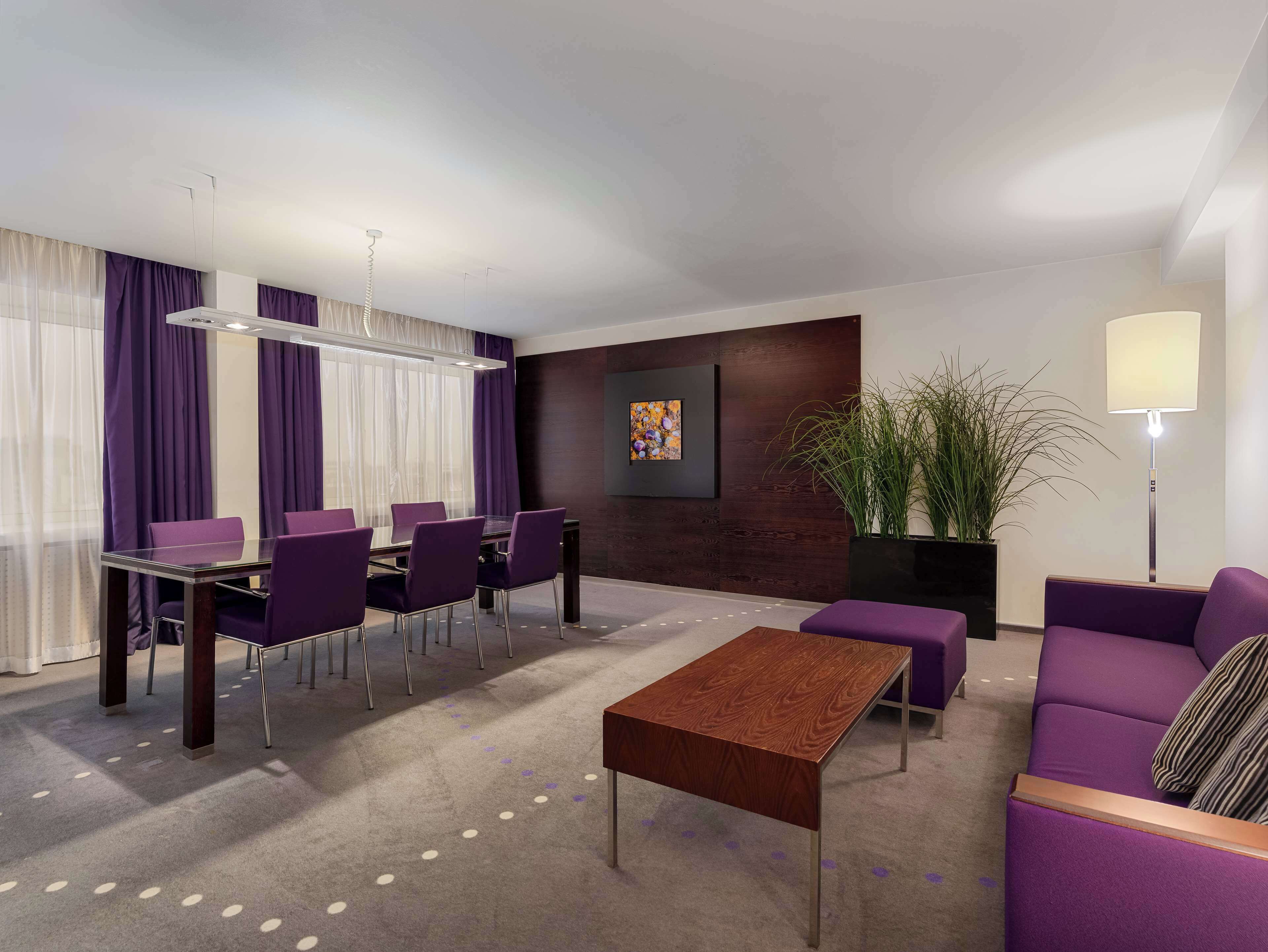 Ett modernt hotellrum med en matplats, en soffa, ett soffbord och en stor krukväxt.