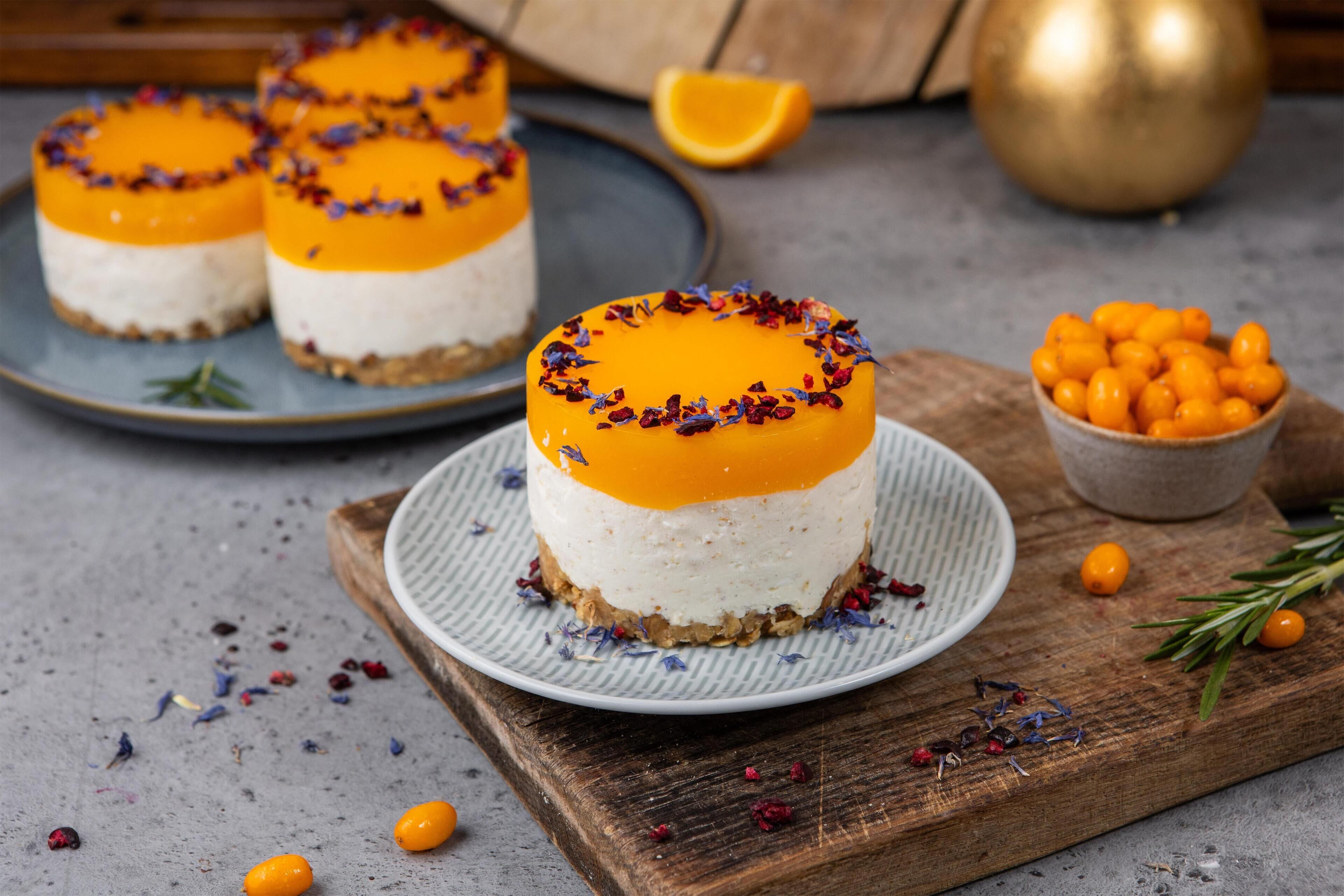 Three round desserts on a plate, with a bowl of small orange fruits and a wooden board in the background.