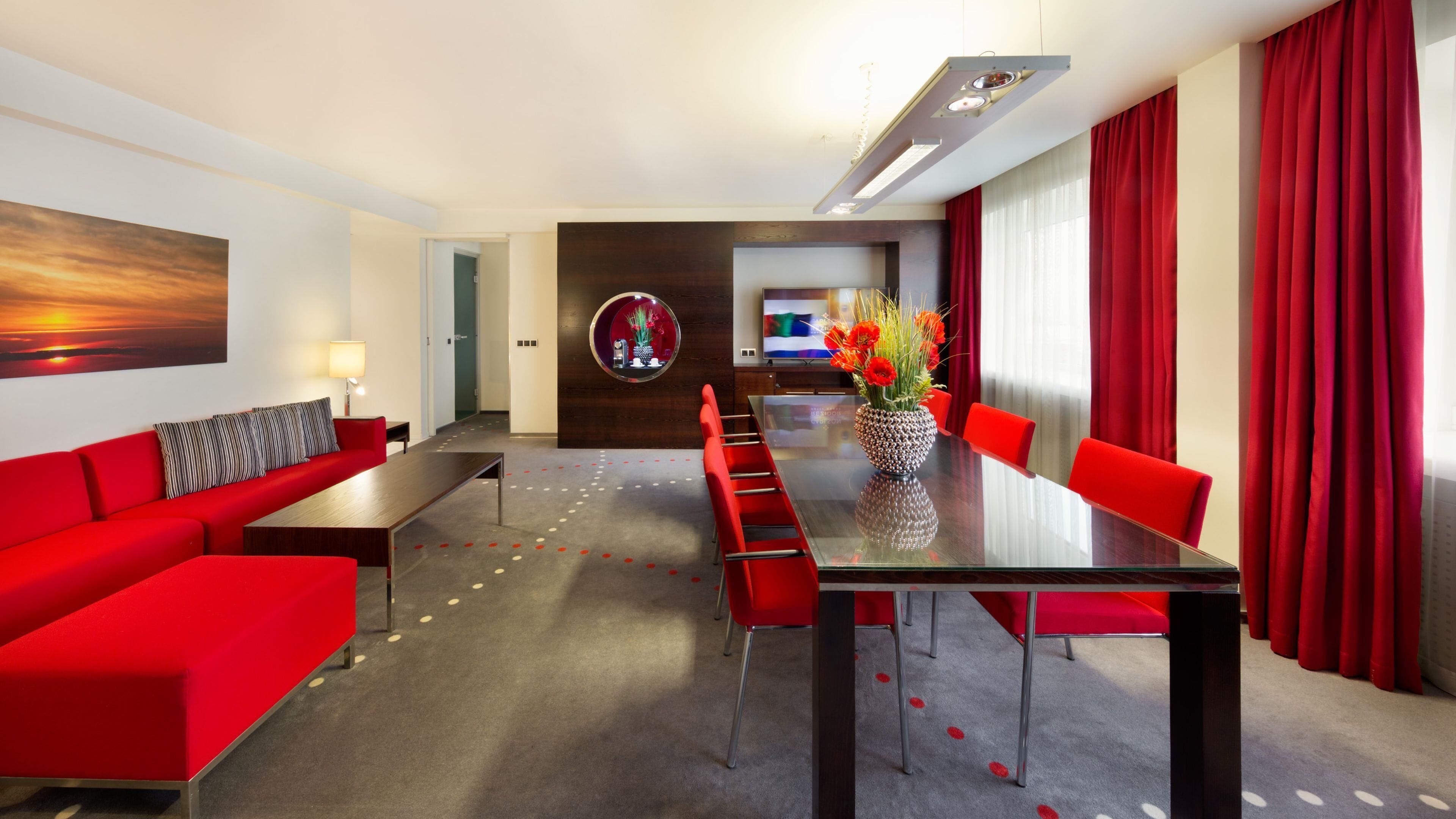 Moderni hotellihuone, jossa on punainen sohva, ruokapöytä ja punainen verho.
