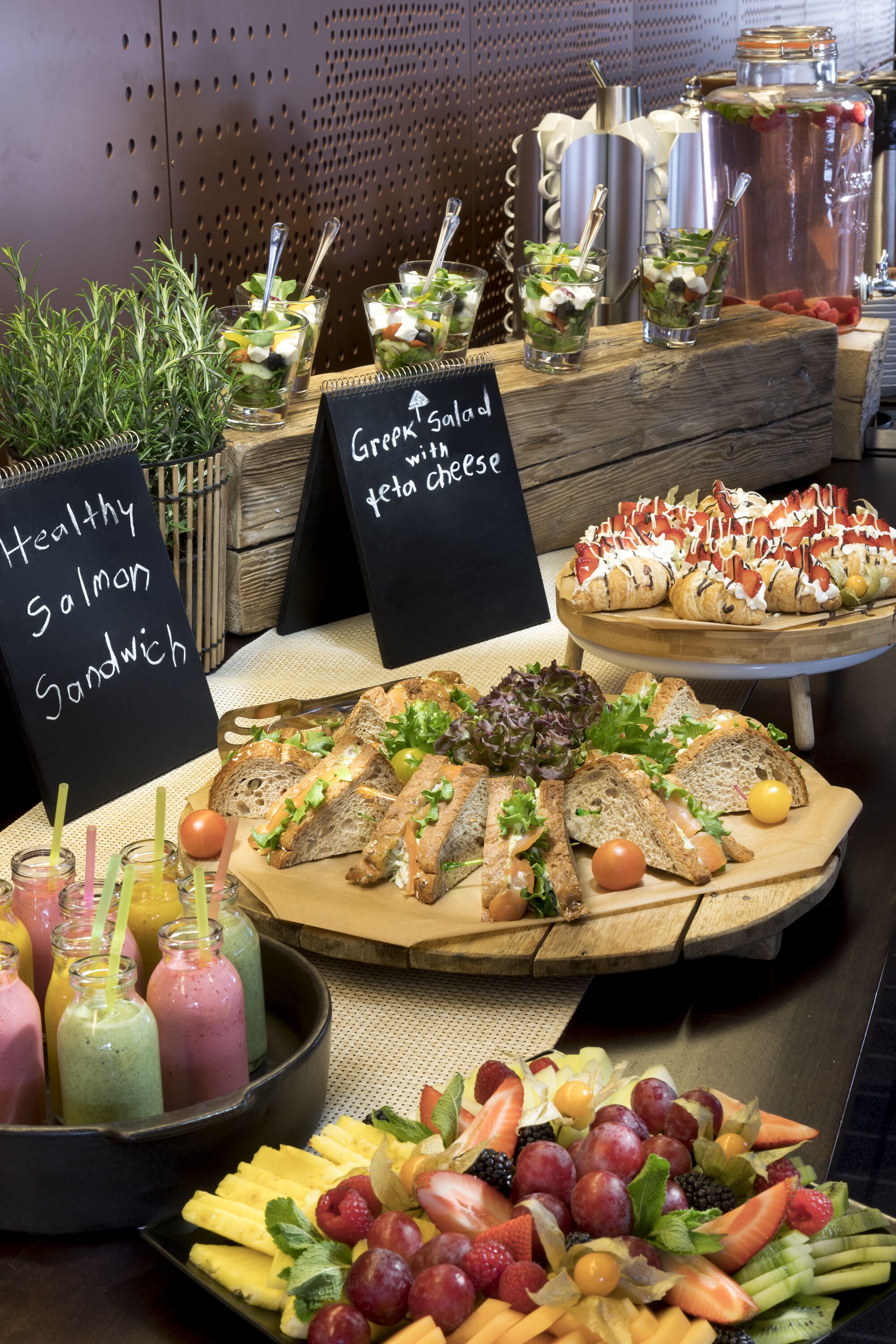 A buffet with various food options including a salmon sandwich, Greek salad with feta cheese, and an assortment of bread and fruits.
