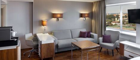 Una habitación de hotel moderna con sofá, sillones, escritorio y televisión.