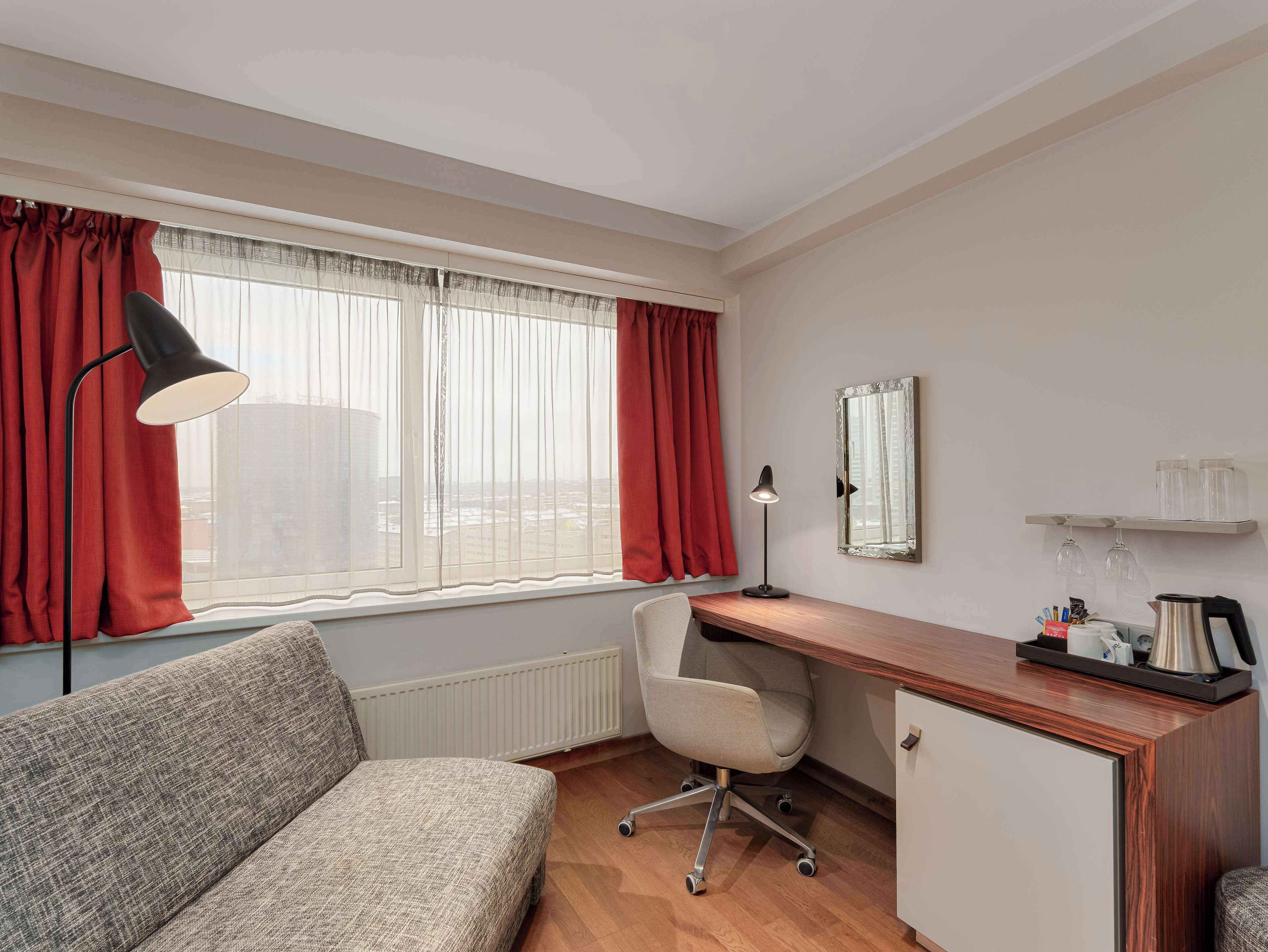 Quarto de hotel com sofá, escrivaninha, cadeira e janela com cortinas.