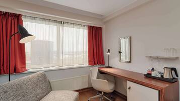 Quarto de hotel com sofá, escrivaninha, cadeira e janela com cortinas.