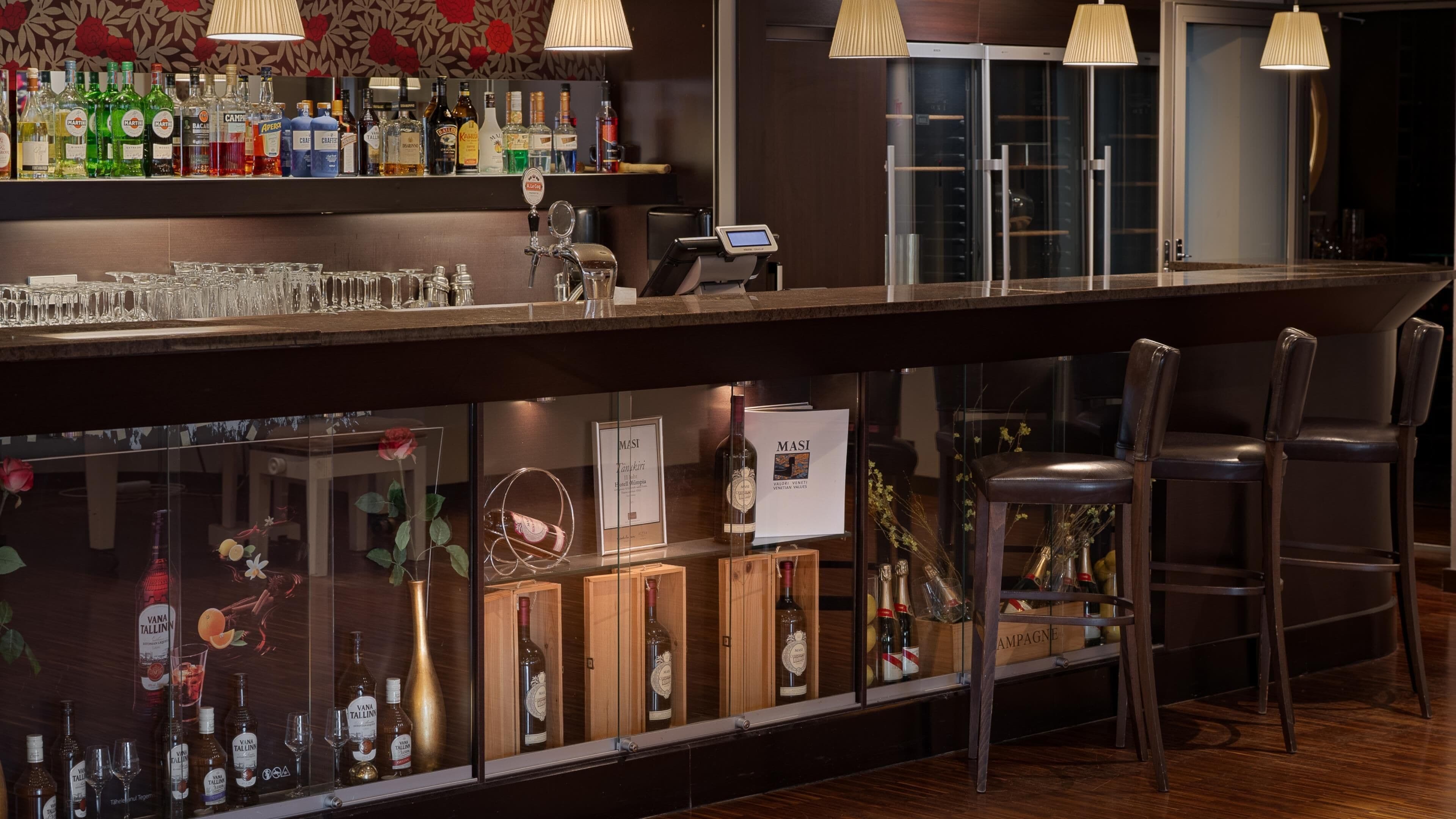 A bar area with a variety of liquor bottles, glasses, and a cash register.