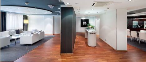 A modern hotel lobby with a reception desk, seating area, and a bar.
