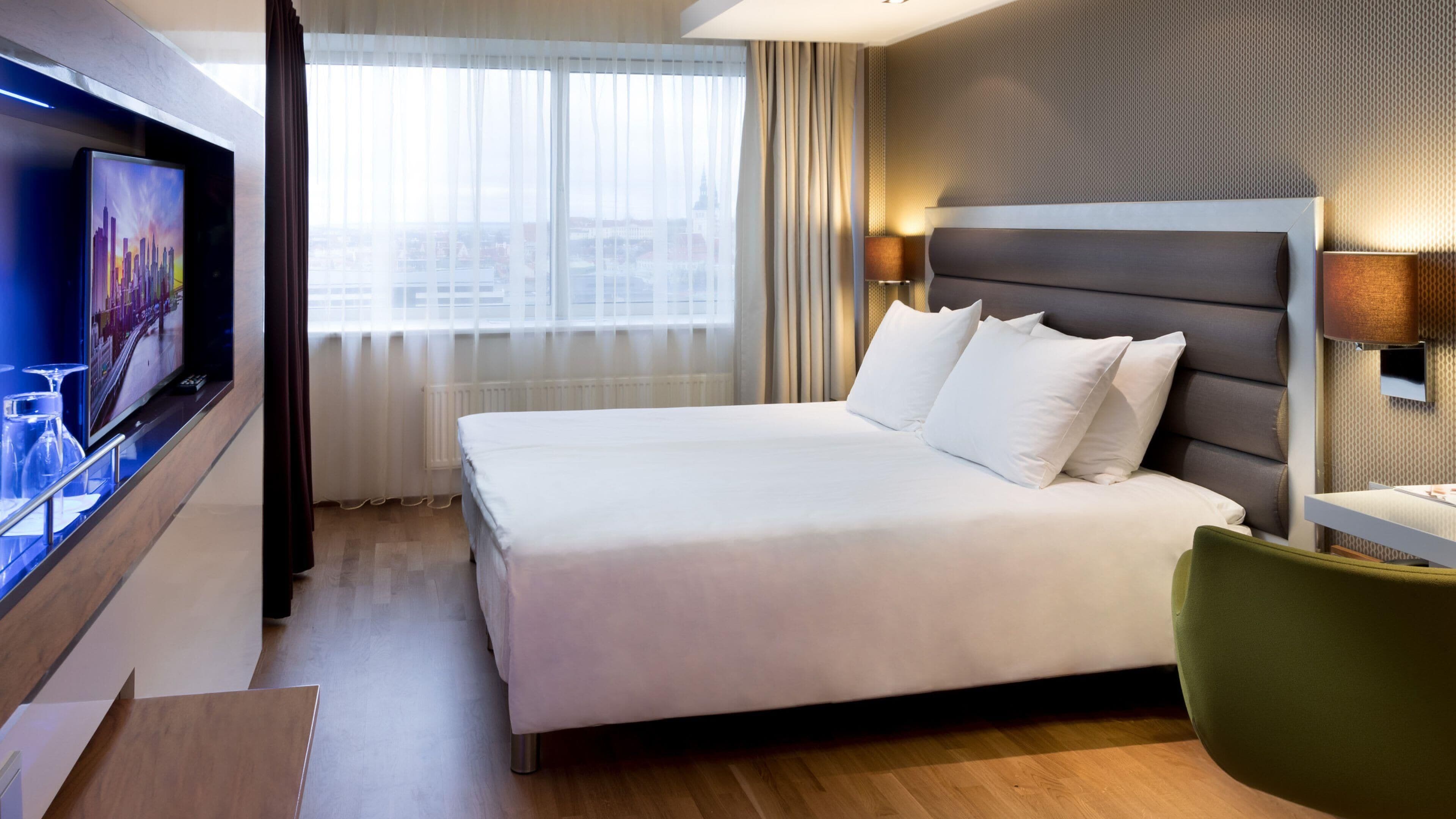 A hotel room with a bed, a TV, a desk, and a chair.