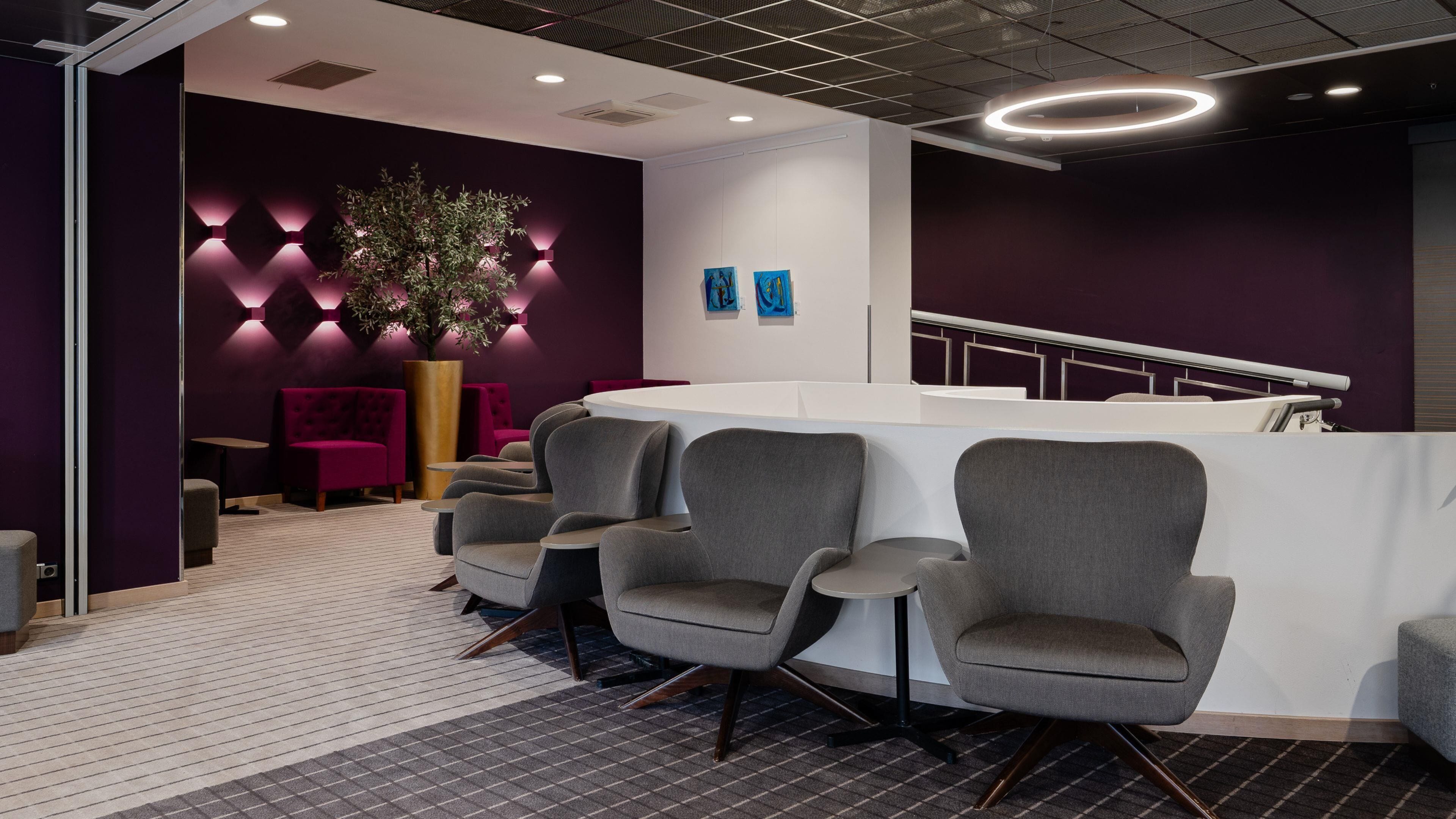 A reception area with a white reception desk, grey chairs, a large potted plant, and purple walls.