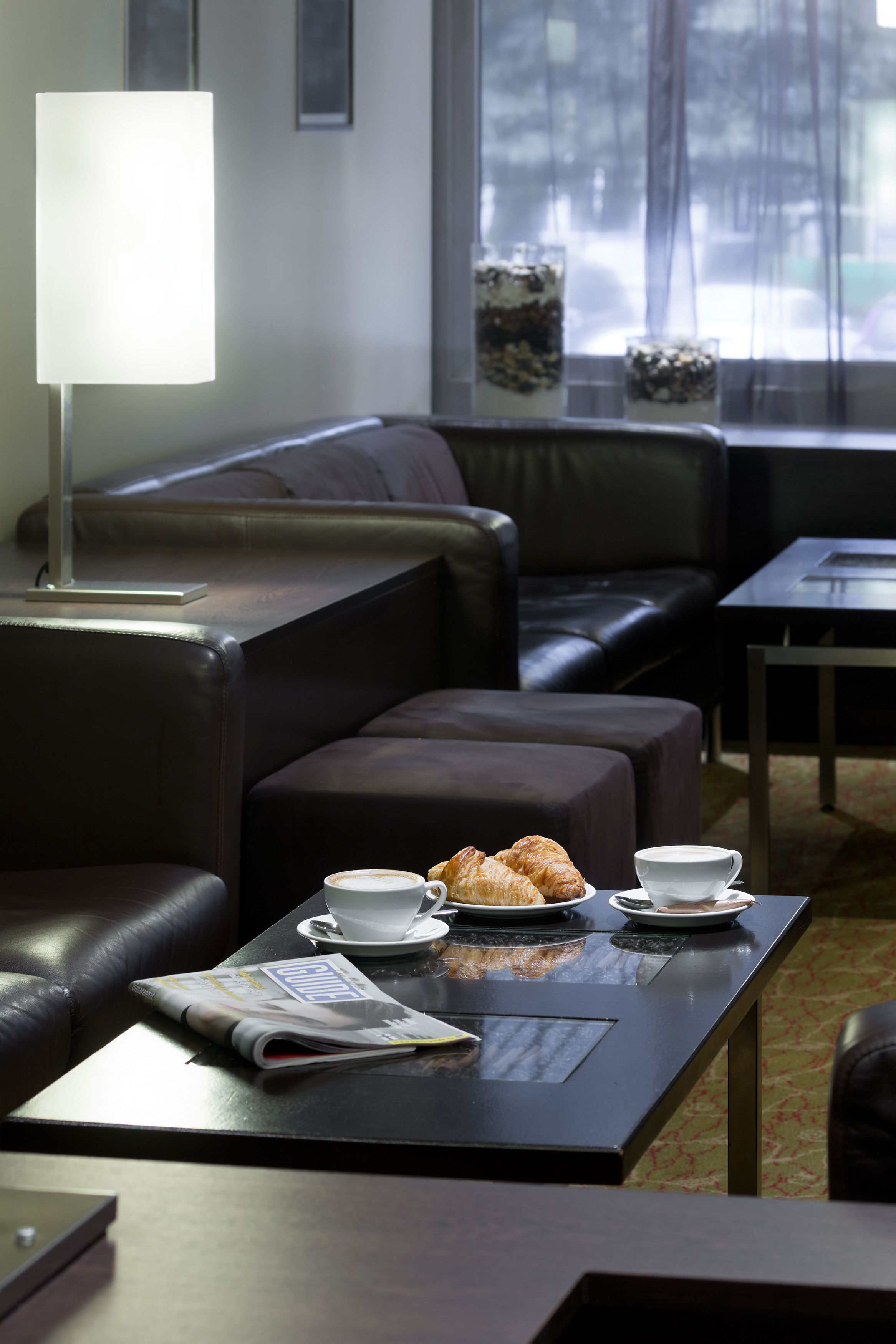 A modern living room with a leather sofa, a coffee table with croissants and cups, and a magazine.