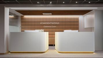 Un moderno centro de convenciones con pared de paneles de madera, dos mostradores de recepción e iluminación empotrada en el techo.