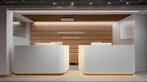 Un moderno centro congressi con una parete rivestita in legno, due banchi di accoglienza e un soffitto con illuminazione a incasso.