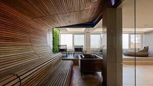 A modern interior with a curved wooden bench, a glass partition, and a view of the city. - Radisson Blu Hotel Olumpia (Tallinn)