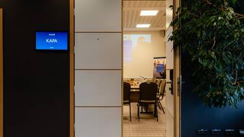 A room with a KAPA sign, a projector screen, a table with chairs, and a plant.