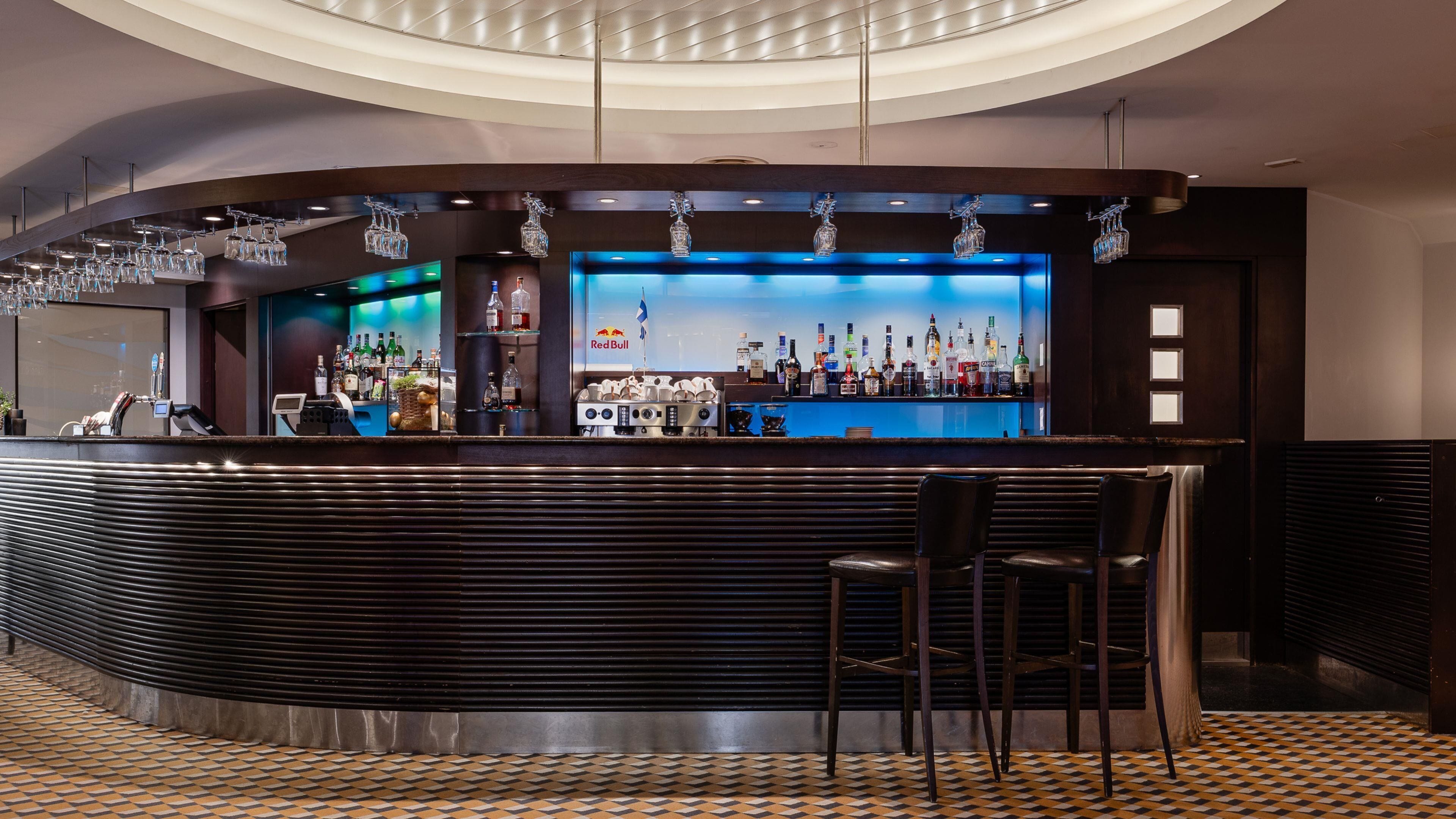 A bar area with a curved counter, bar stools, and a variety of liquor bottles.