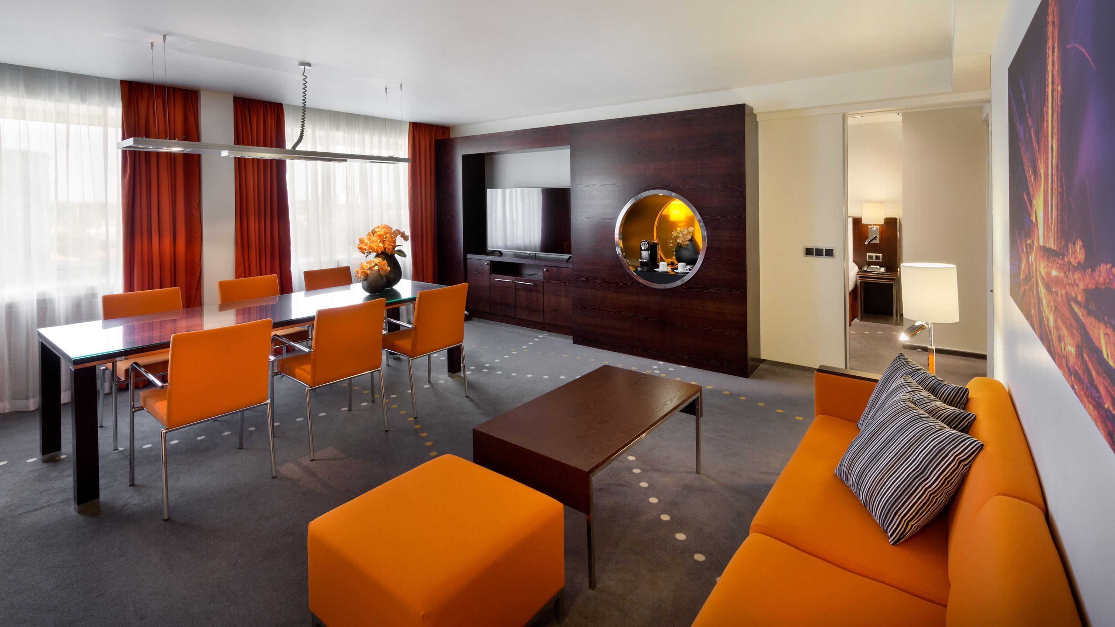 Una habitación de hotel moderna con zona de comedor, un sofá y una televisión.