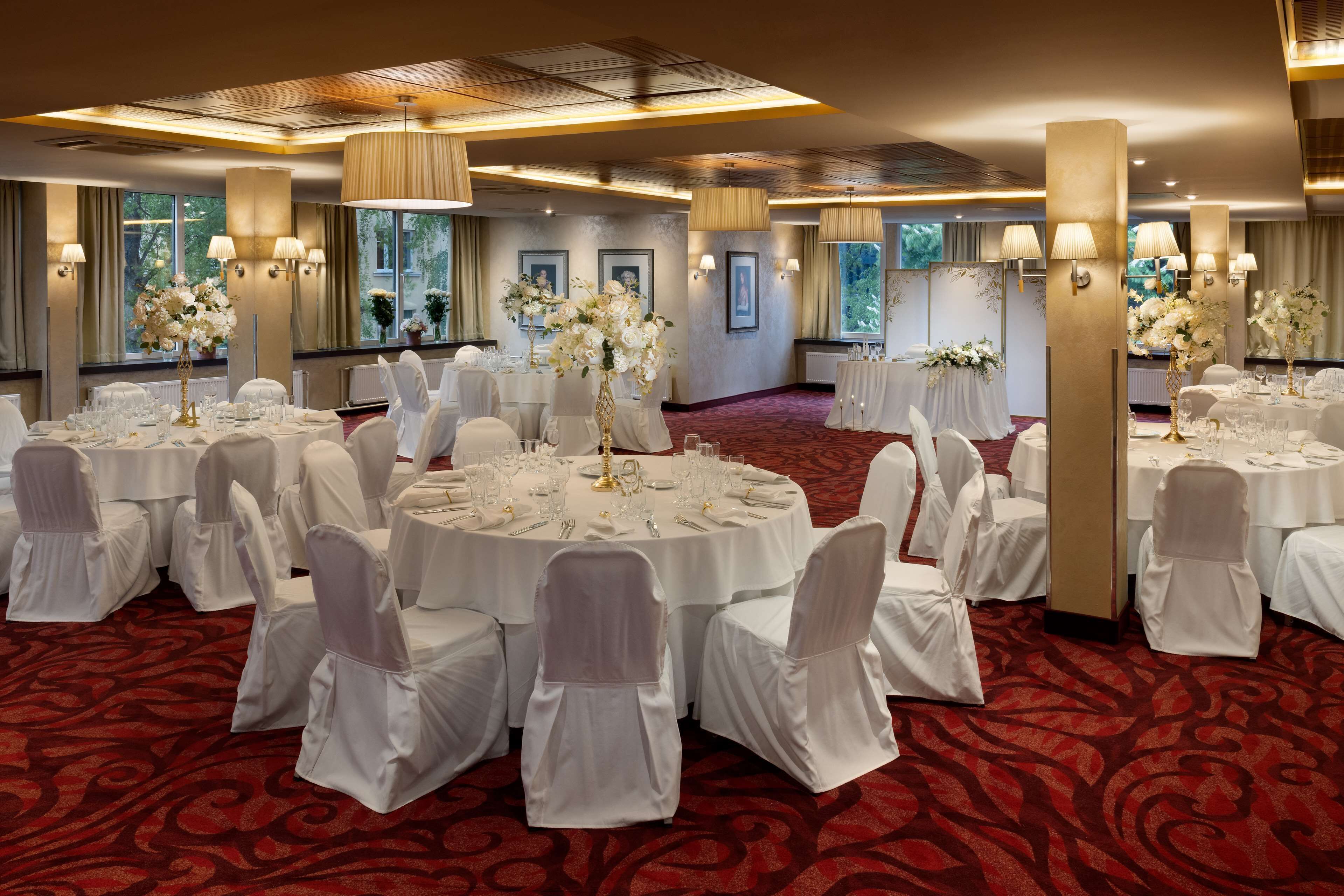 A banquet hall with round tables, white chairs, and floral centerpieces.