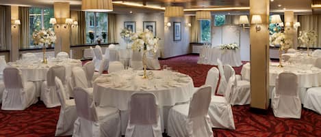 A banquet hall with round tables, white chairs, and floral centerpieces.