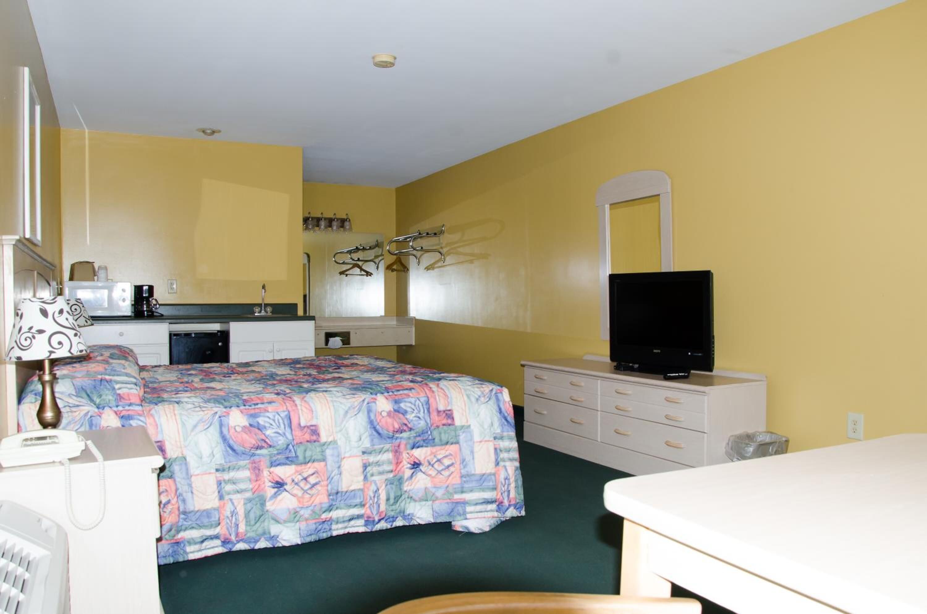 A hotel room with a bed, a desk, a chair, a television, a dresser, and a mirror.