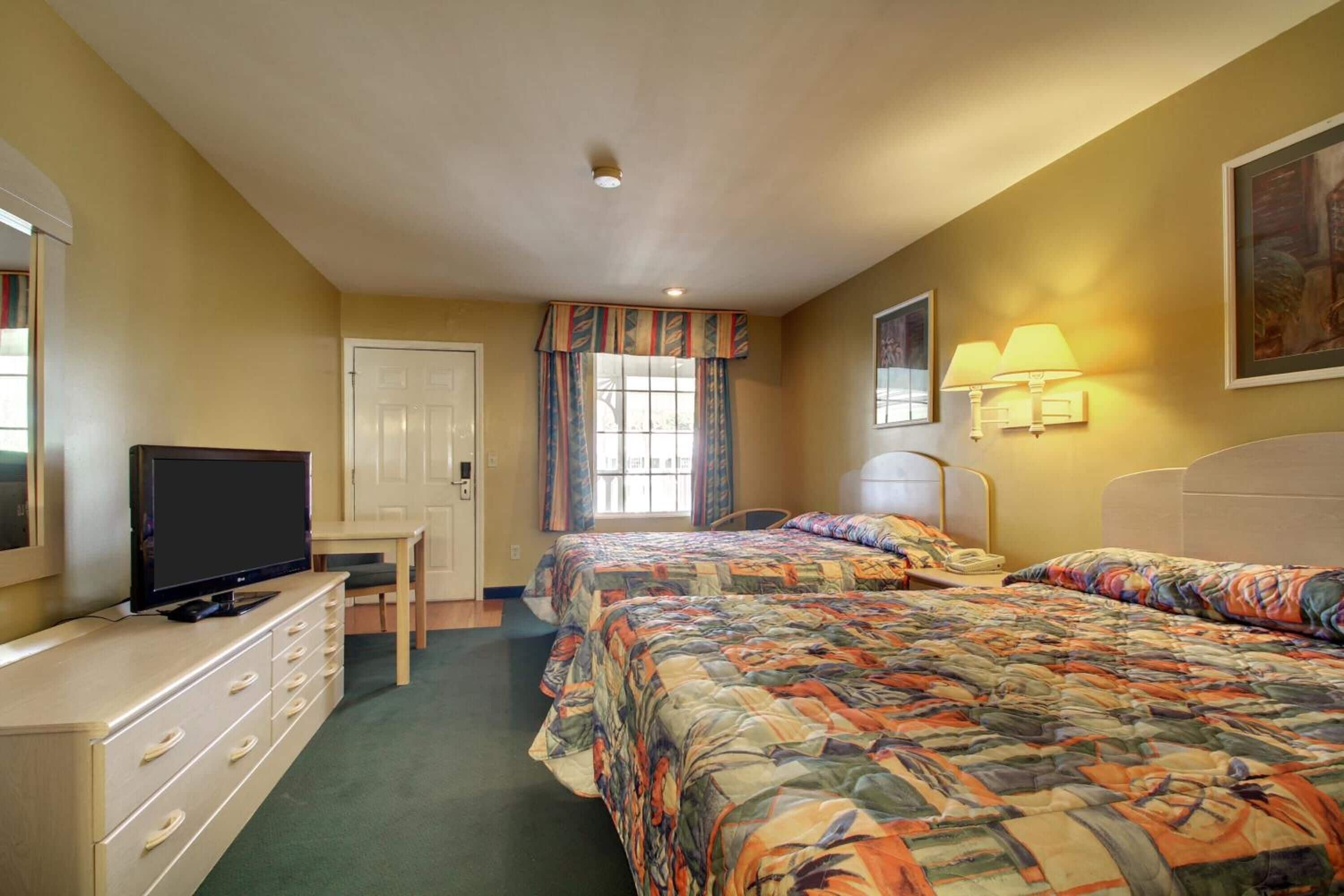 A hotel room with two beds, a television, a desk, and a window with curtains.