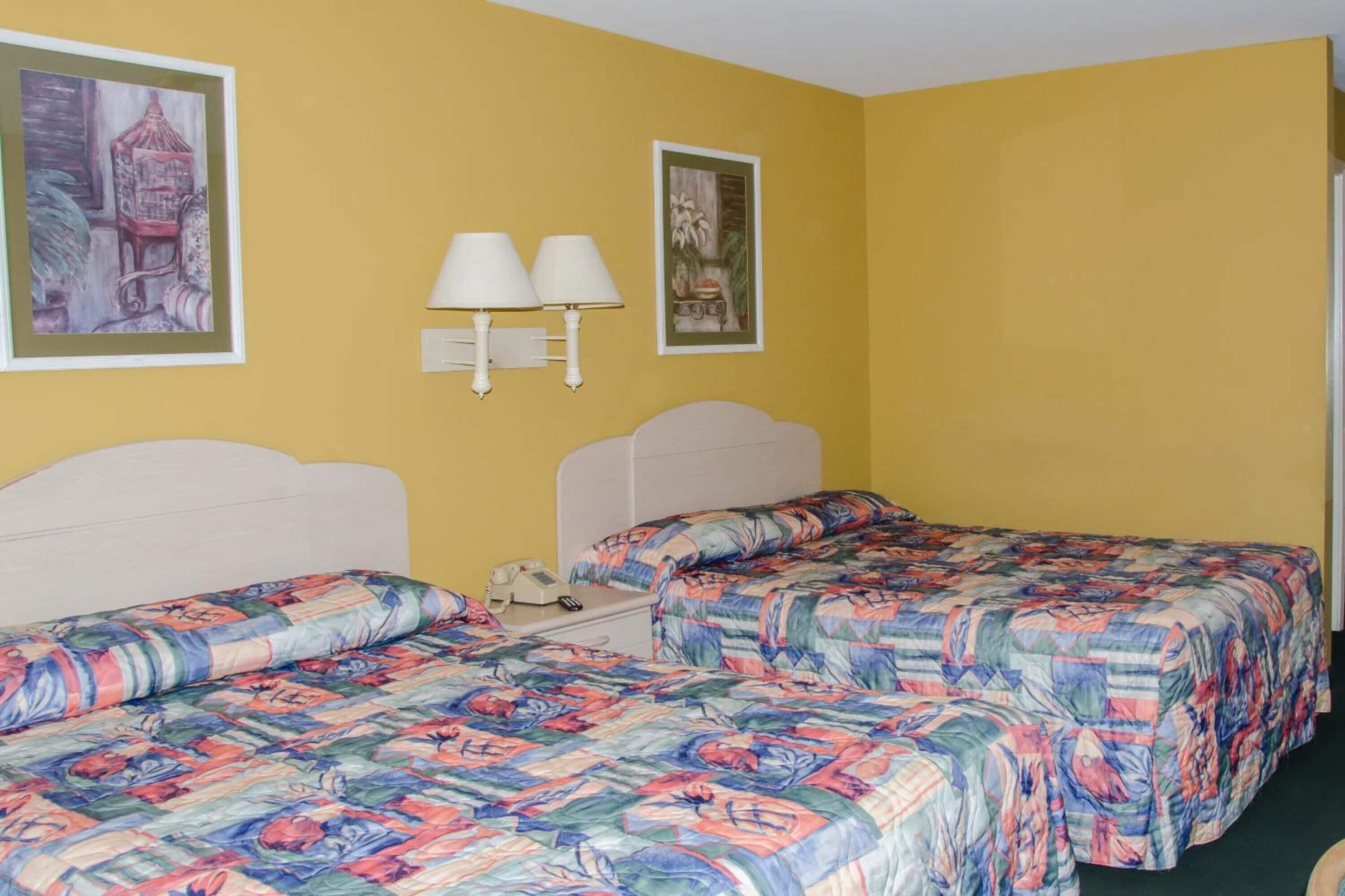 A hotel room with two beds, each with floral-patterned bedding, a white headboard, and a nightstand with a lamp.