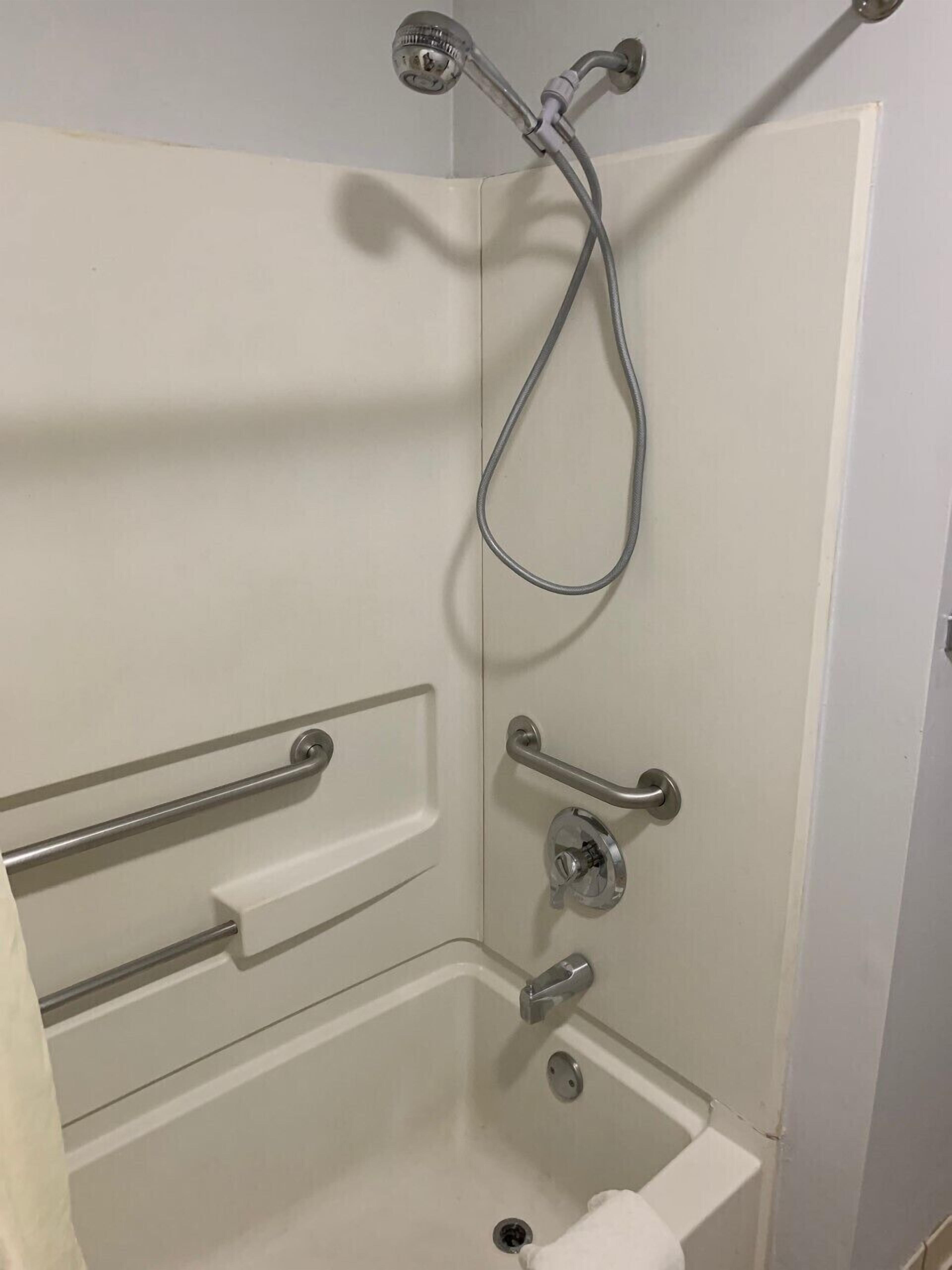Una ducha a nivel con barra de apoyo, cabezal de ducha de mano y un perchero.