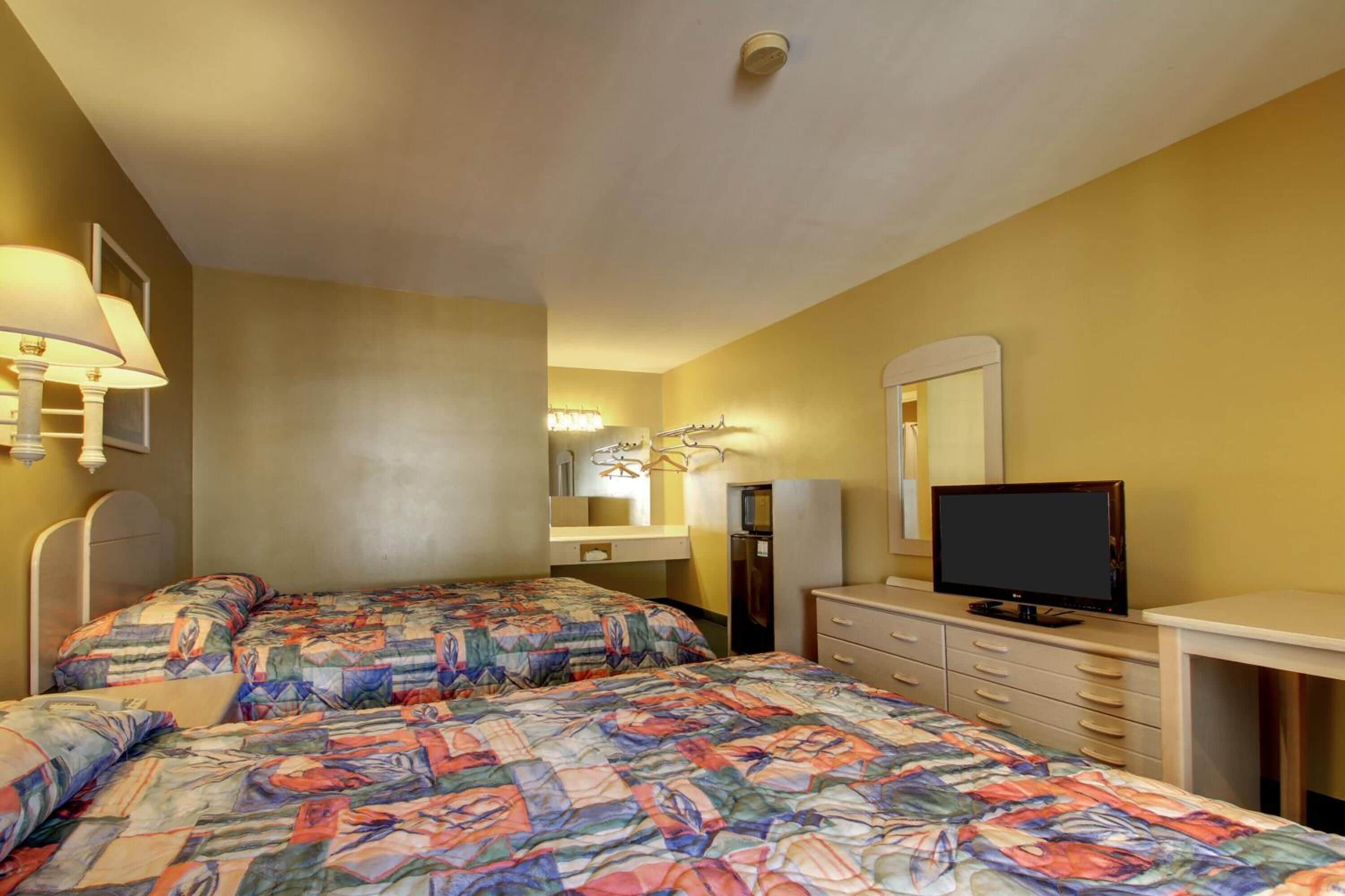 Una habitación de hotel con dos camas, televisión, escritorio y espejo.