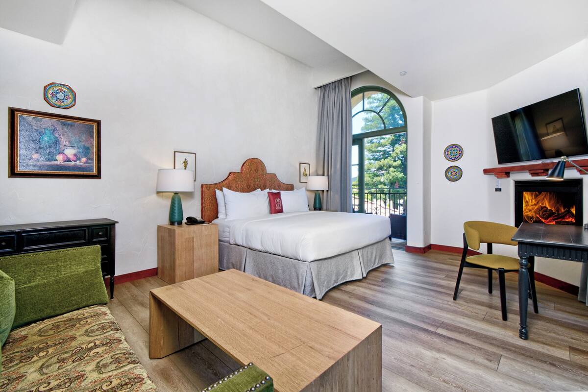 A hotel room with a bed, a desk, a chair, a TV, and a fireplace.