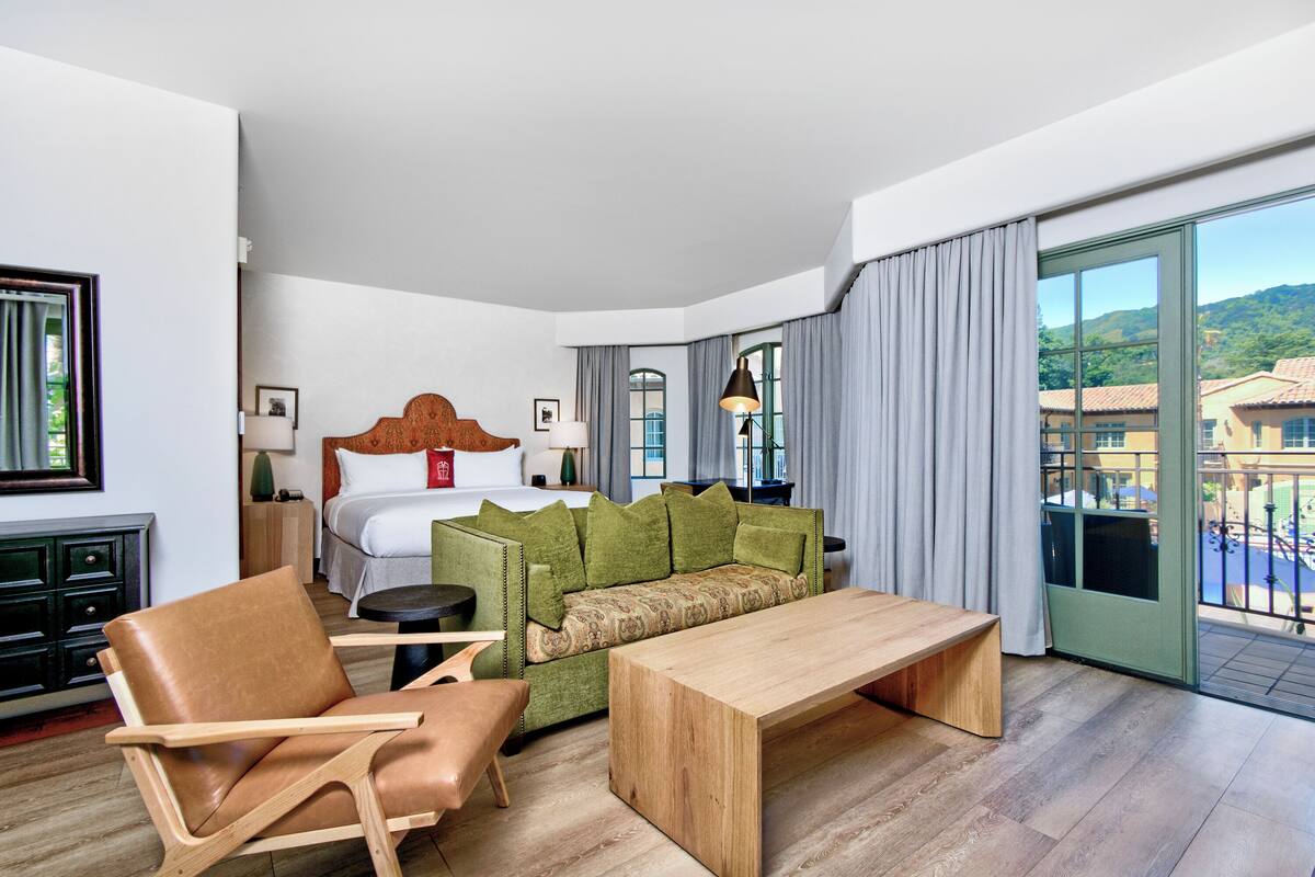A hotel room with a bed, a green sofa, a wooden table, and a chair.