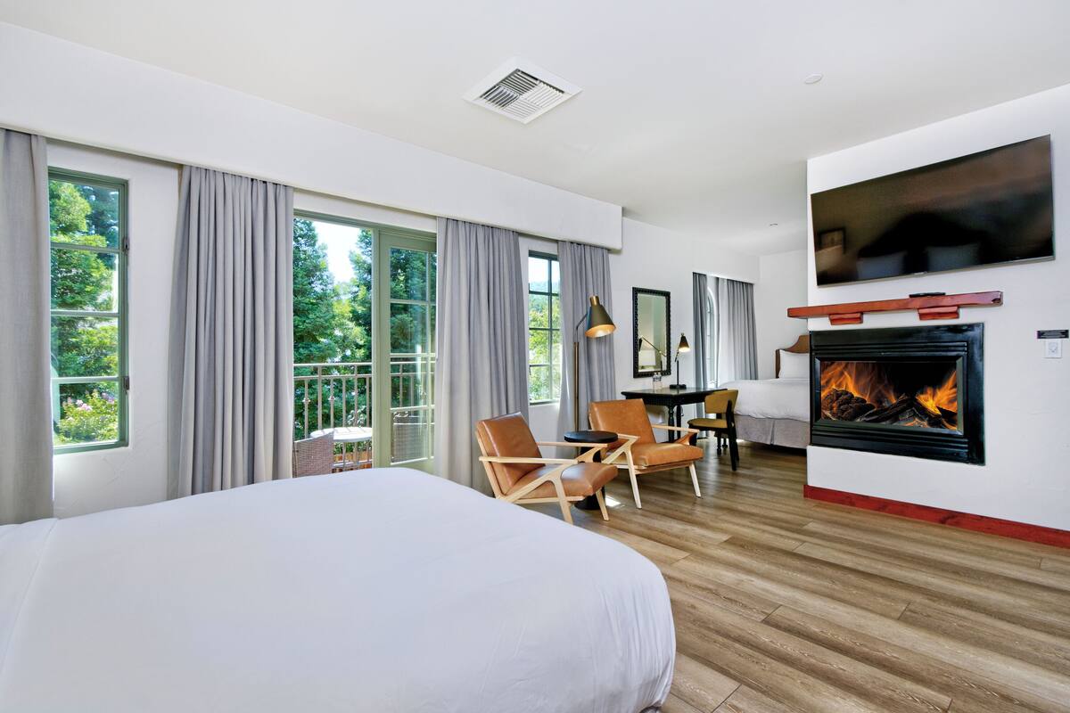 A hotel room with a large bed, a fireplace, a television, and a balcony with curtains.