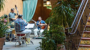Una escalera con detalles ornamentales en cerámica, un músico sentado tocando la guitarra, y una persona de pie sosteniendo un bajo.