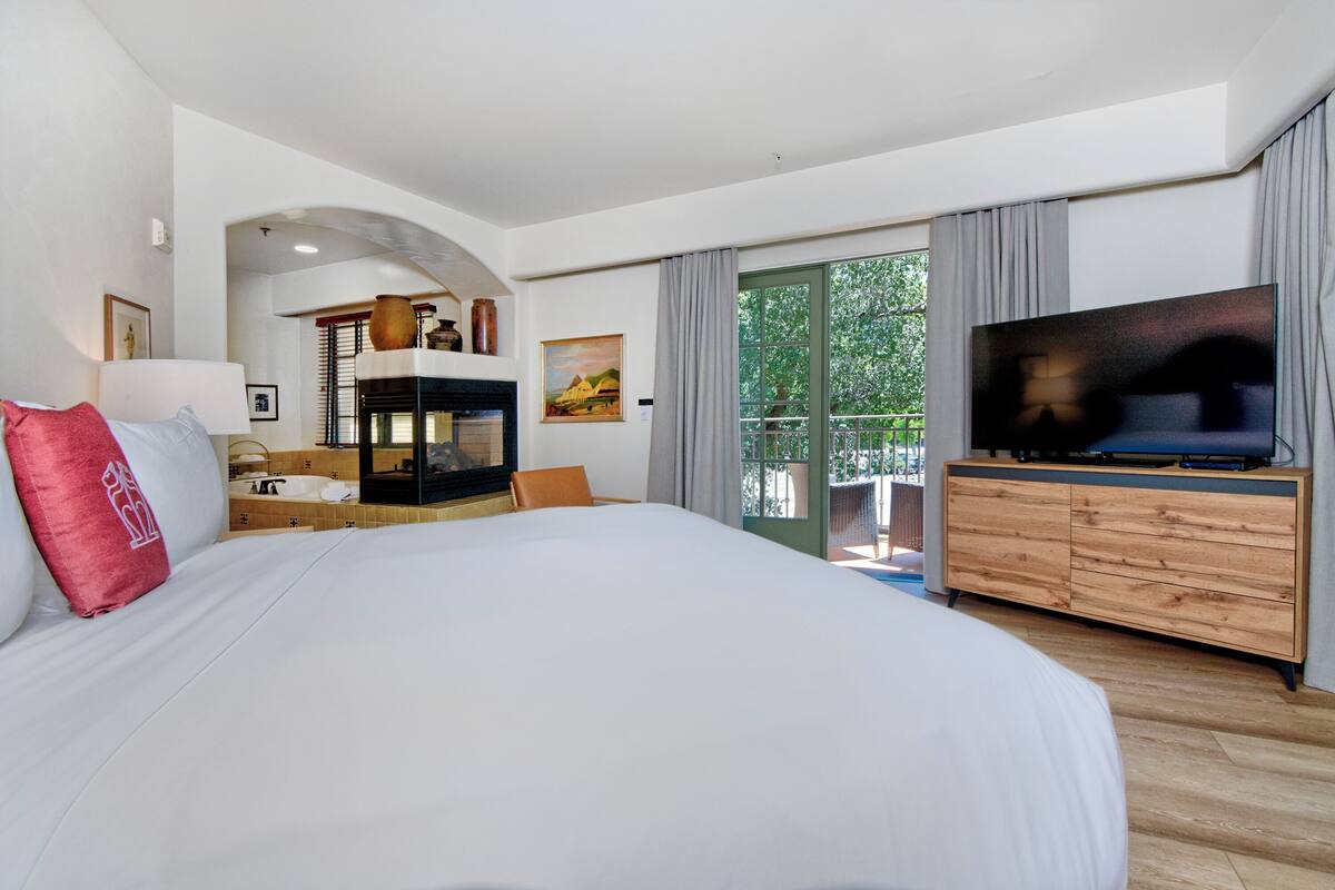 A spacious bedroom with a large bed, a TV, and a balcony with a view.
