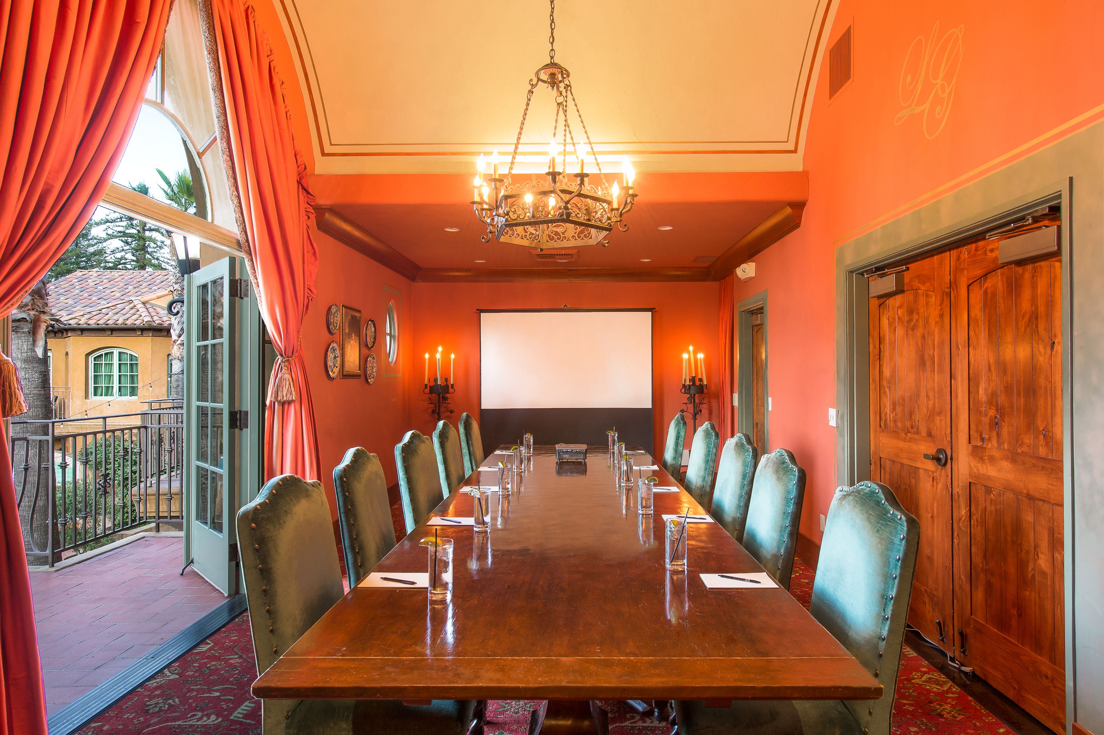 Une salle de conférence avec une longue table, des chaises, un écran de projection et un lustre.