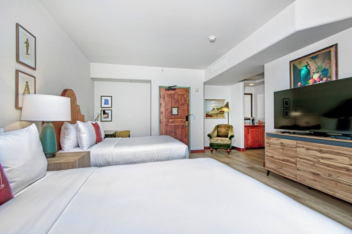 A hotel room with two beds, a TV, a wooden dresser, and a door leading to a bathroom.
