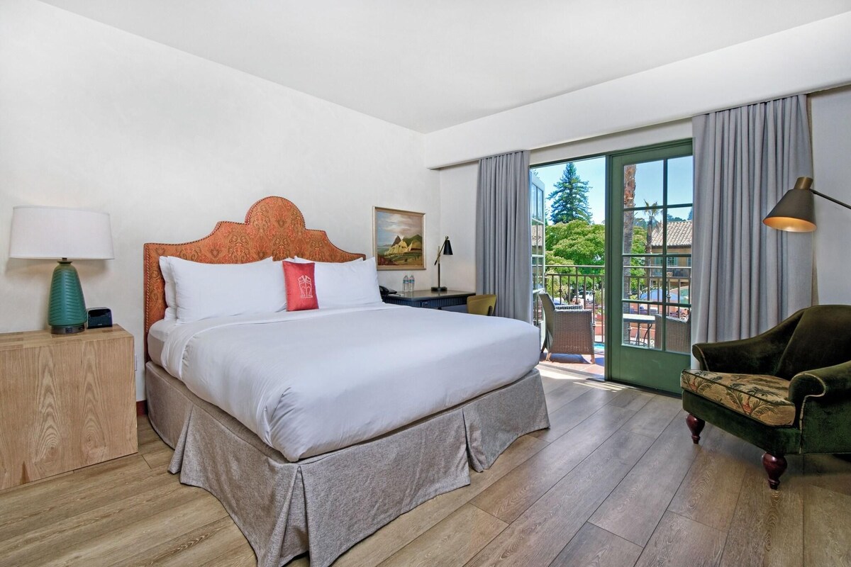 Habitación de hotel con una cama grande, una mesita de noche, una silla y vistas al exterior.