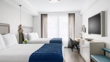 A hotel room with two beds, a desk, a TV, and a large window with curtains.