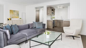 A modern living room with a grey sofa, a glass coffee table, and a white armchair.