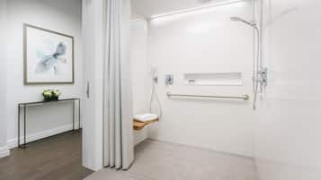 A modern bathroom with a shower, a toilet with a towel rack, a small shelf, and a framed picture on the wall.