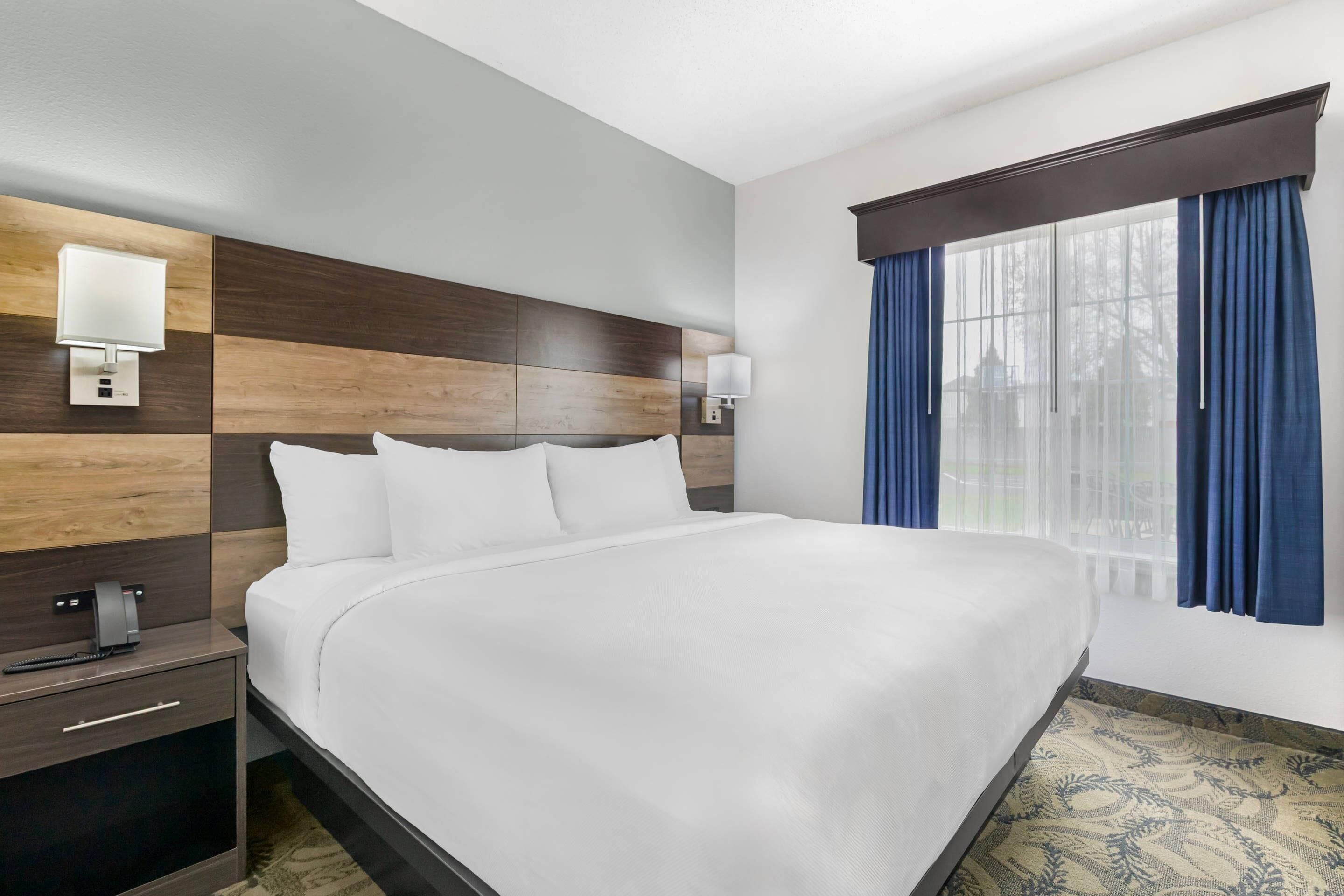 A hotel room with a large bed, a nightstand with a lamp, and a window with curtains.