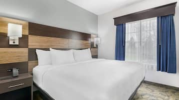 A hotel room with a large bed, a nightstand with a lamp, and a window with curtains.