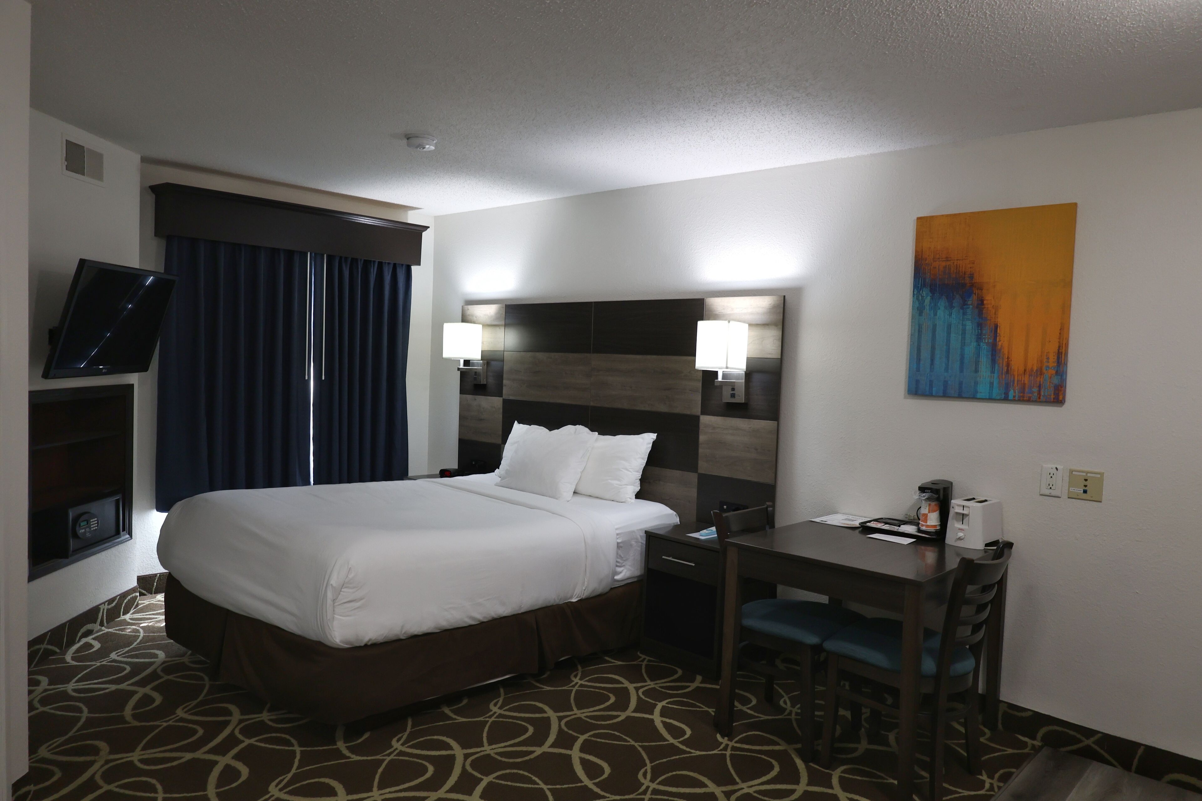A hotel room with a large bed, a desk with a chair, a television, and a painting on the wall.